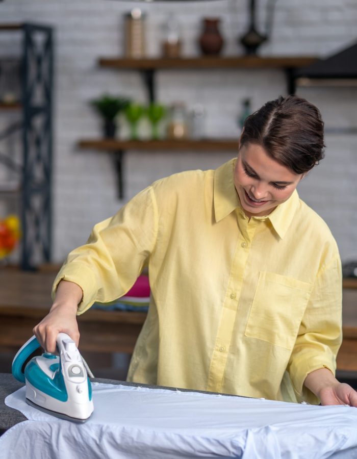 Waist-up portrait of a smiling pleased dark-haired female smoothing out wrinkles on a piece of clothing